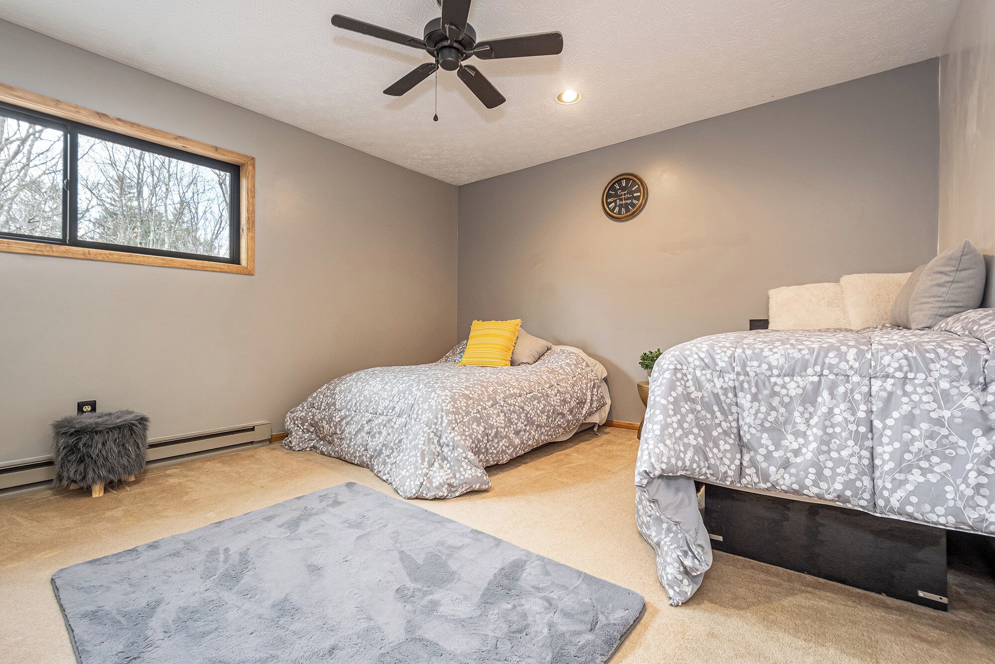 A bedroom with two beds, a ceiling fan, a clock, and a window.