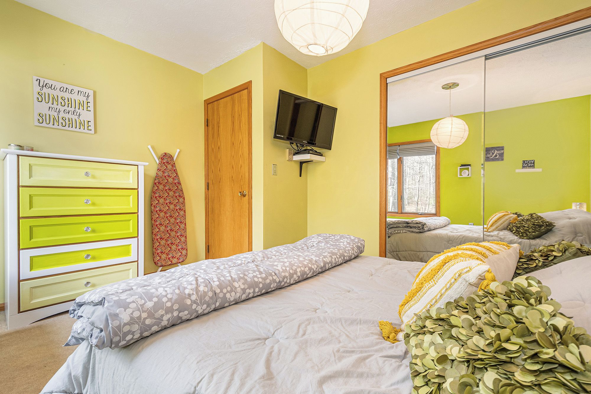 A bedroom with a bed, a dresser, a television, and a mirror.