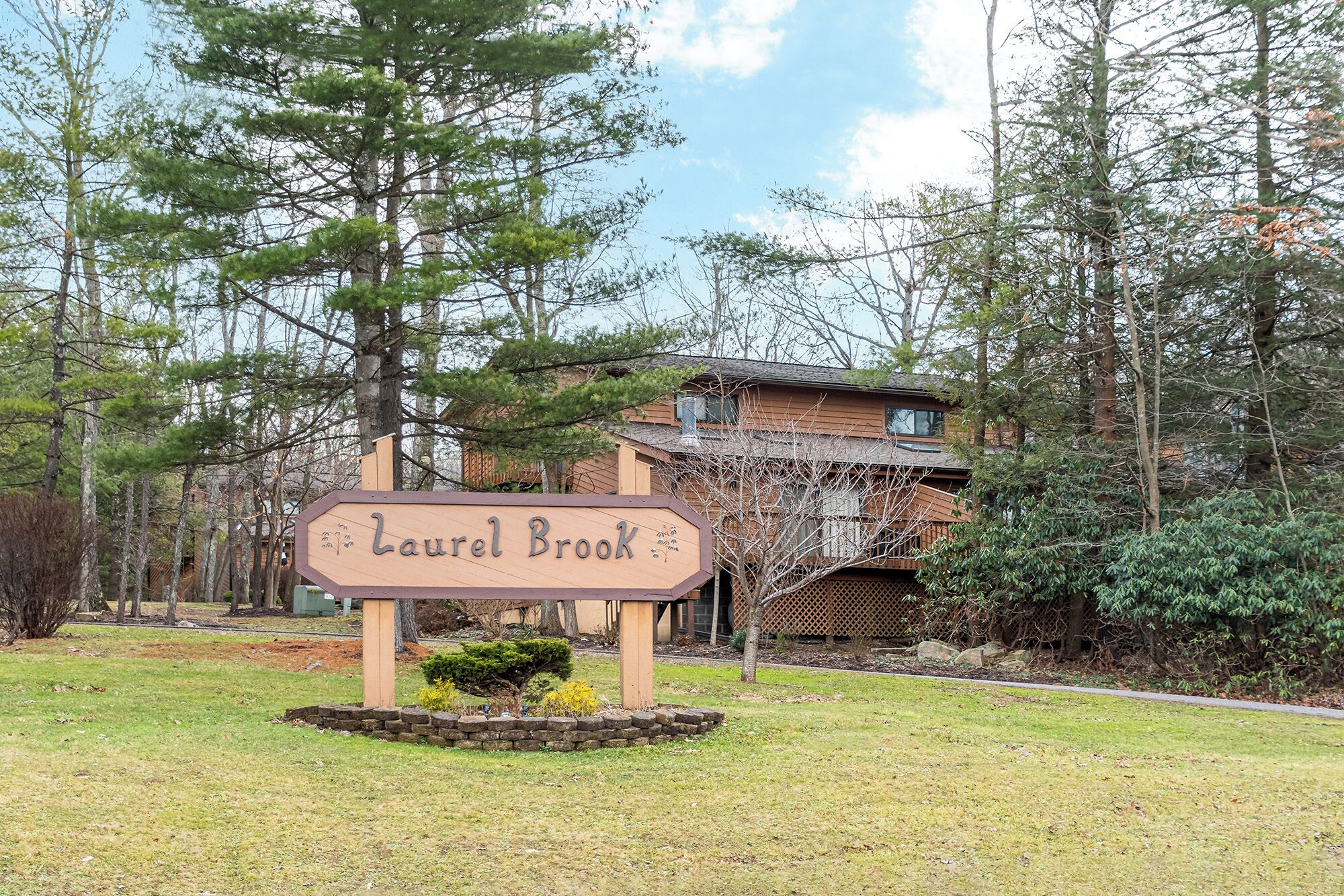 A wooden sign with the text "Laurel Brook" in front of a building surrounded by trees.