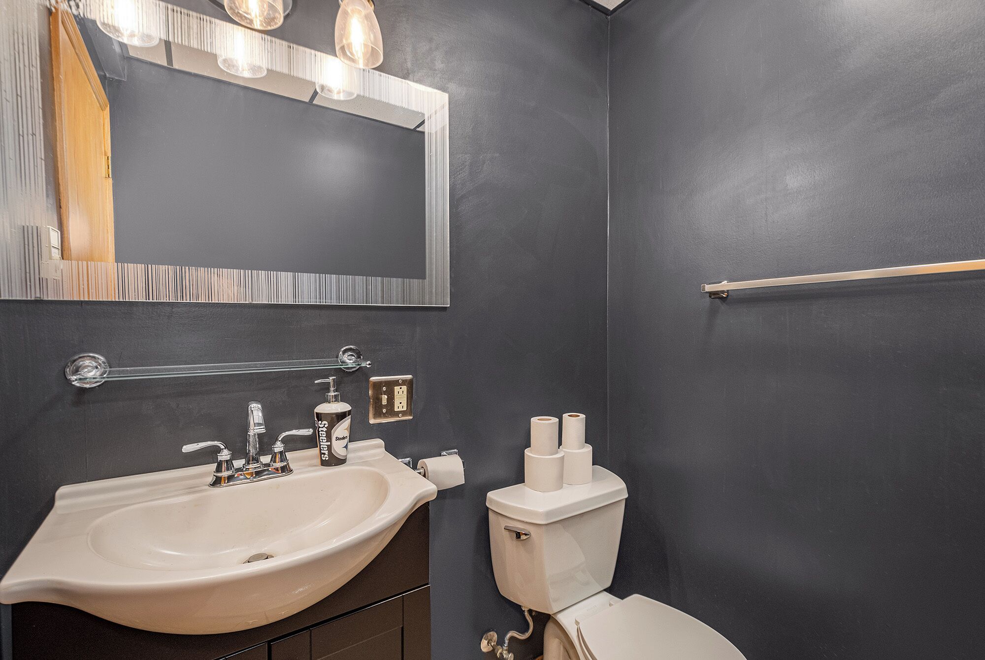 A bathroom with a beige sink, a toilet, and a mirror with lights.