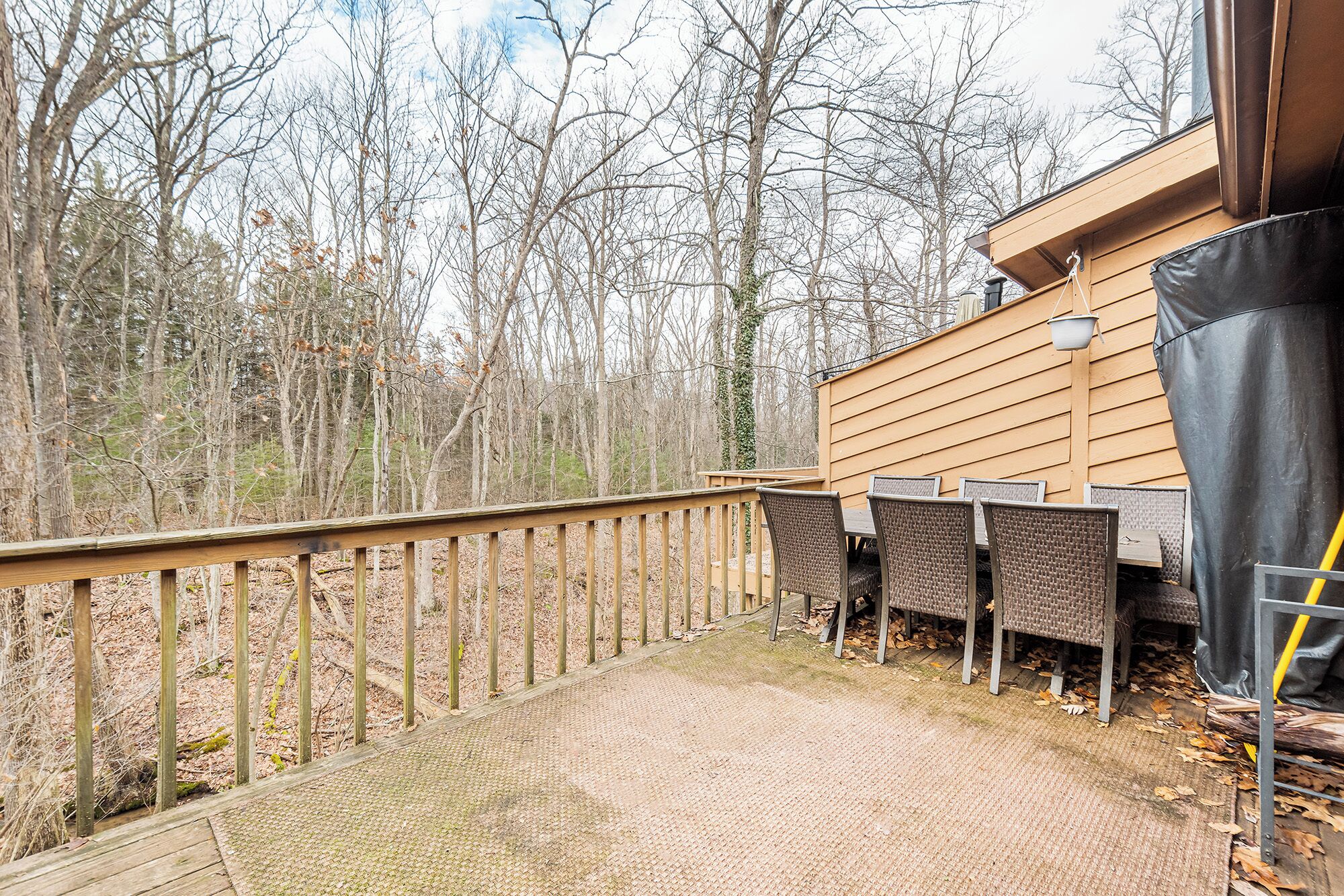 A wooden deck with a metal railing, wicker chairs, and a table.