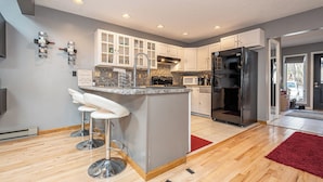 A modern kitchen with white cabinets, a central island with bar stools, a stainless steel refrigerator, and a microwave. - Laurel Brook 39 by Taylor Made Deep Creek (Oakland)