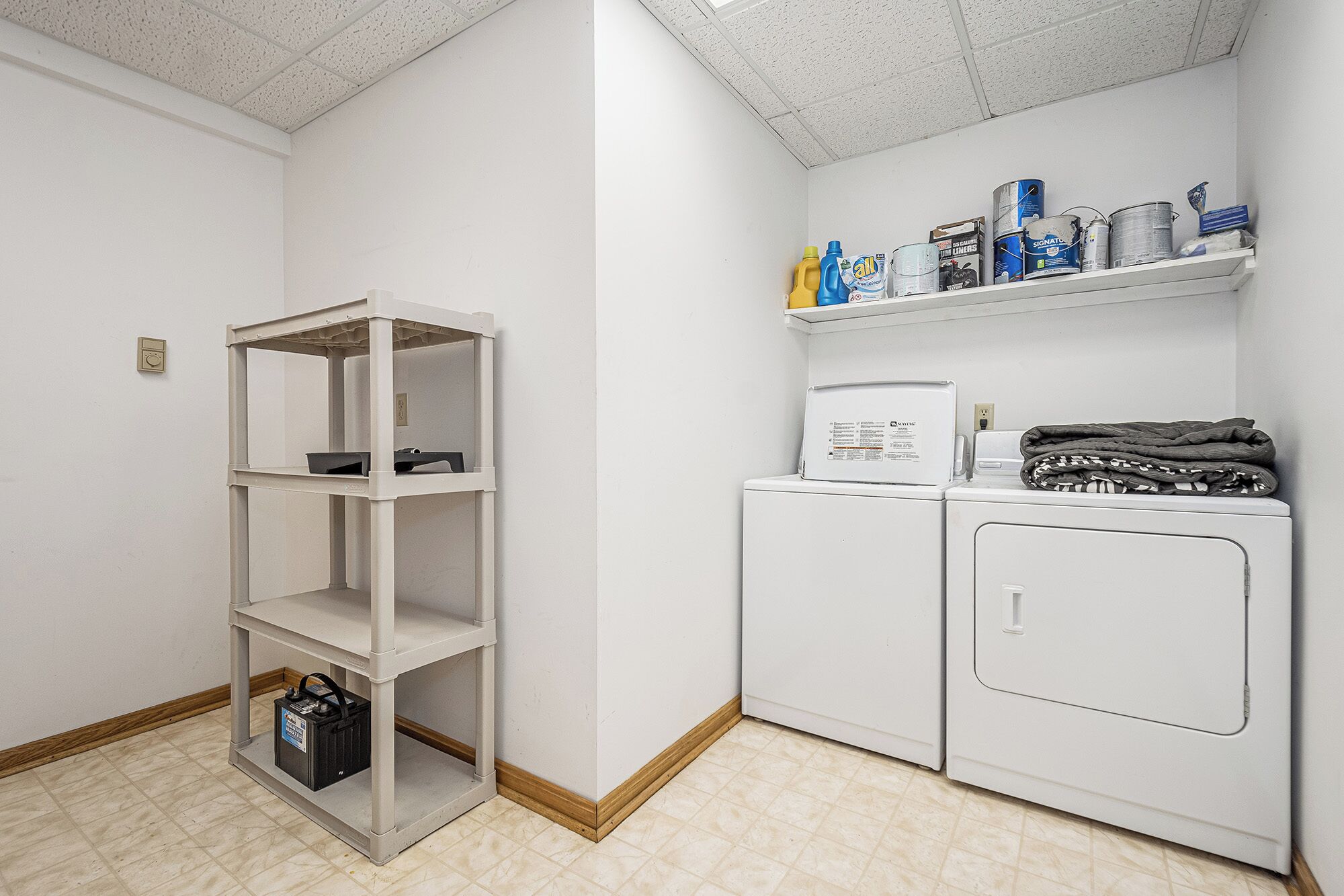 A laundry room with a washing machine, dryer, and shelves with cleaning supplies.