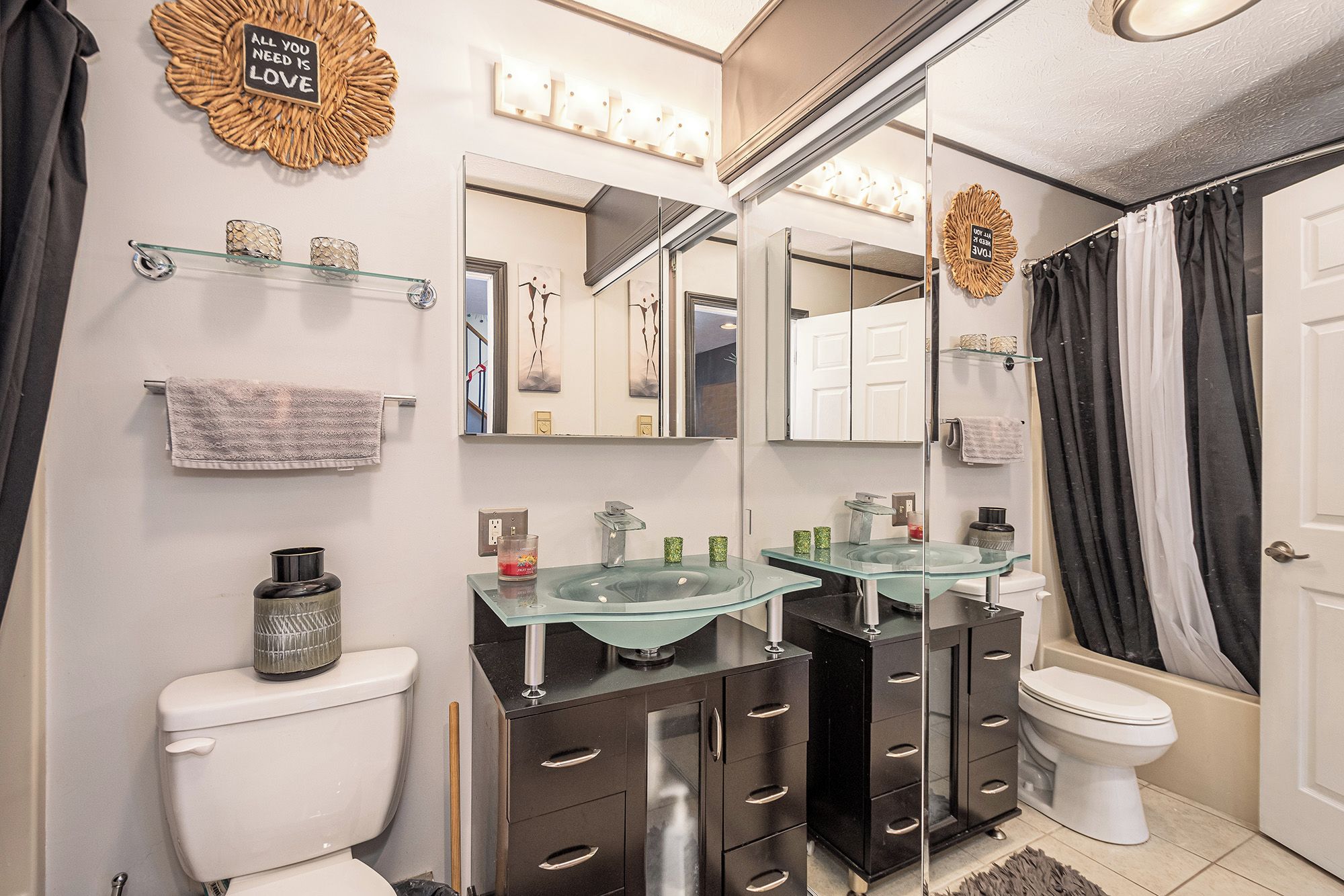 A modern bathroom with two glass sinks, dark cabinetry, a white toilet, and a shower curtain.