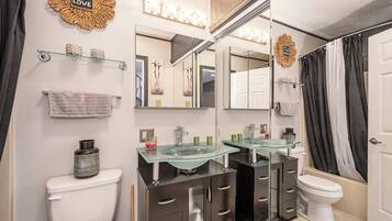 Une salle de bain moderne avec deux vasques en verre, des meubles de rangement sombres, des toilettes blanches et un rideau de douche.
