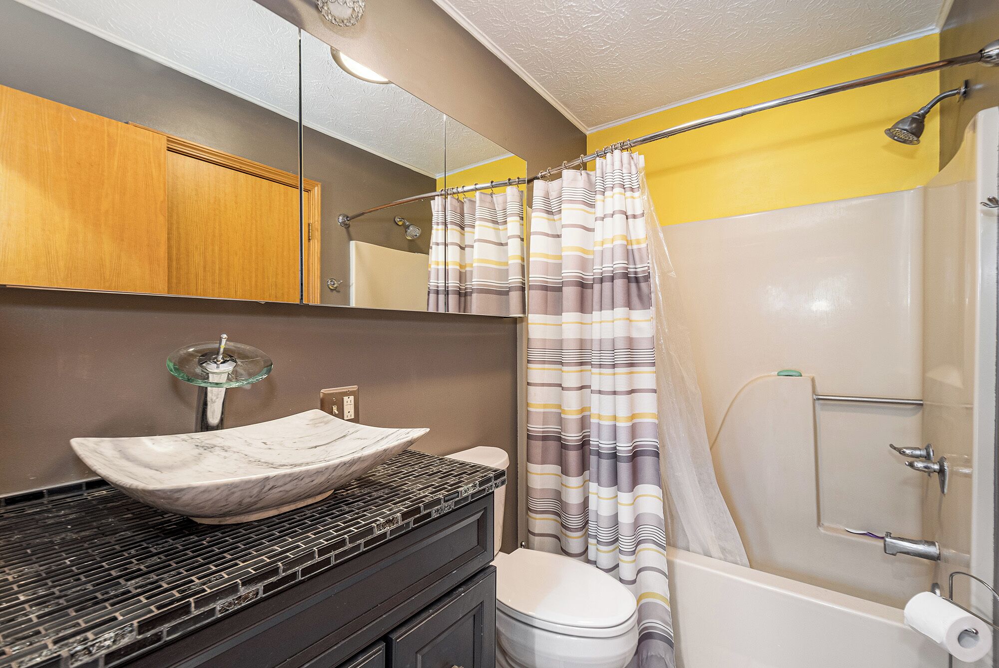 A bathroom with a marble sink, a toilet, a shower with a striped curtain, and a mirror above the sink.