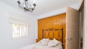 A bedroom with a wooden headboard, a bed with white linens, a window with blinds, and a chandelier. - Cubo's Ideal Alhaurin Job / urban / ideal for teleworking (Alhaurín el Grande)