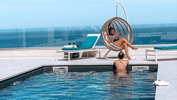 A poolside area with a hanging chair, a lounge chair, and a pool.