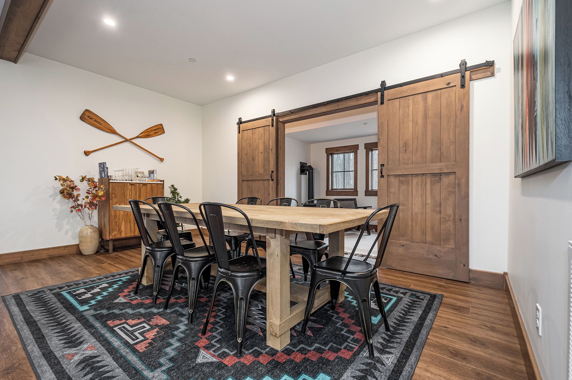 A dining area with a wooden table and chairs, a rug, and a sliding barn door.