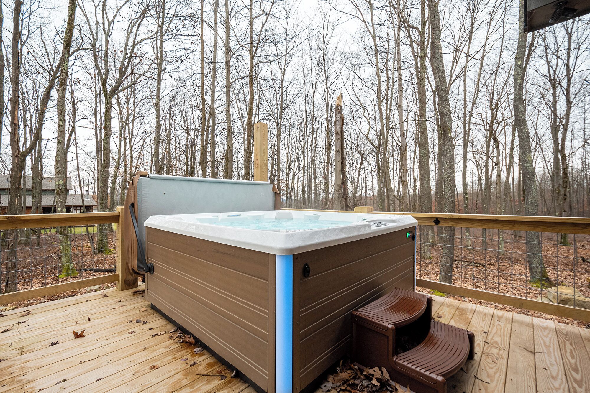 A hot tub on a wooden deck with a view of leafless trees in the background.