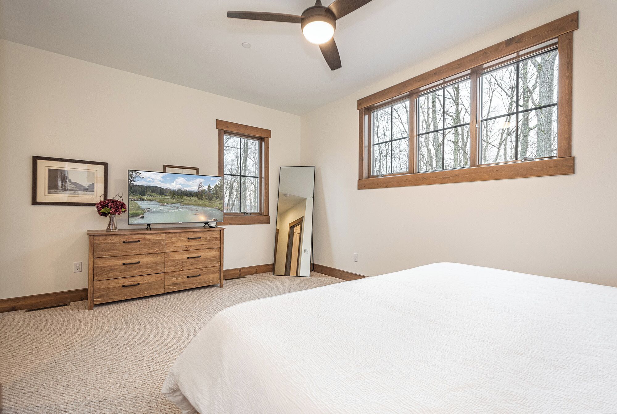 A bedroom with a large bed, a dresser, a television, and a ceiling fan.