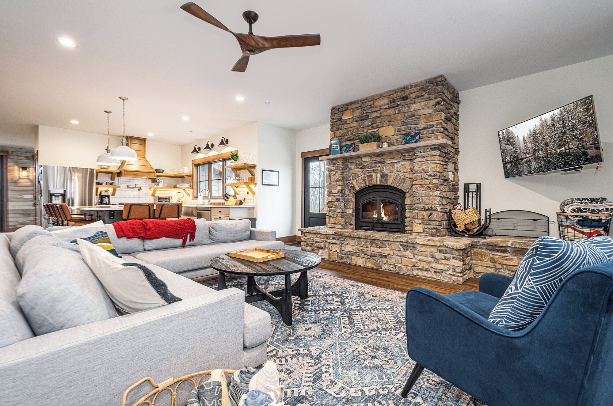 A cozy living room with a stone fireplace, a sofa, a blue armchair, and a dining area in the background.