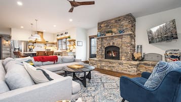 A cozy living room with a stone fireplace, a sofa, a blue armchair, and a dining area in the background.