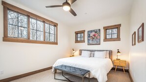 Ein Schlafzimmer mit einem Bett, zwei Nachttischen, einer Bank und drei Fenstern.