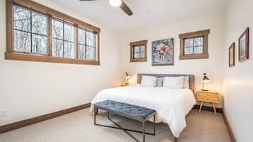 A bedroom with a bed, two bedside tables, a bench, and three windows.