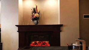 A fireplace with a vase of flowers, a wooden mantel, and a black rug. - Dege Shandi Hotel (Dege)