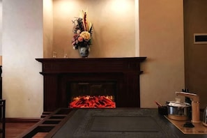 A fireplace with a vase of flowers, a wooden mantel, and a black rug. - Dege Shandi Hotel (Dege)