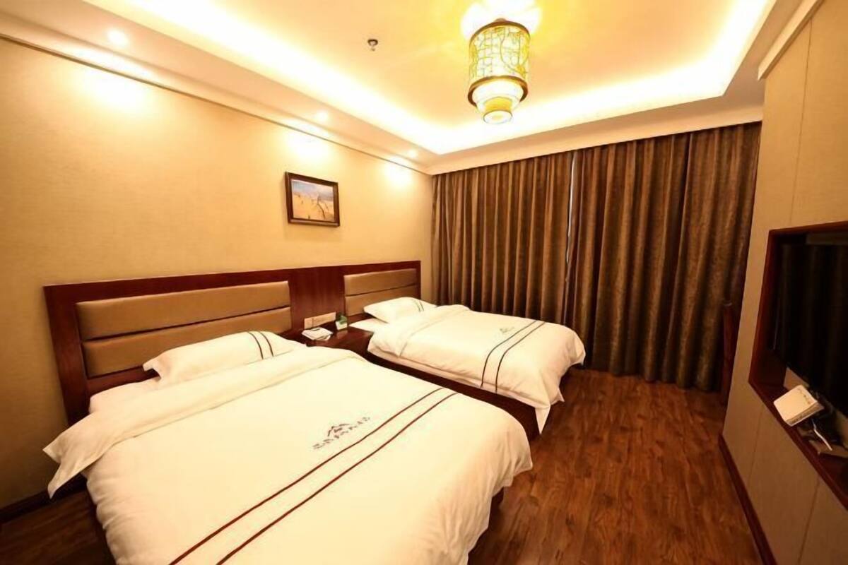 A hotel room with two beds, a flat-screen TV, a nightstand, and a lamp.