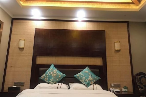 A hotel room with a bed, two wall-mounted lamps, and a headboard with a wooden panel.