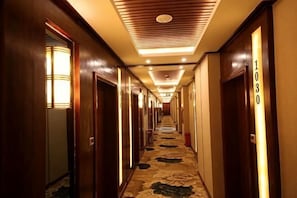 A hotel hallway with wooden doors, numbered room signs, and a patterned carpet.