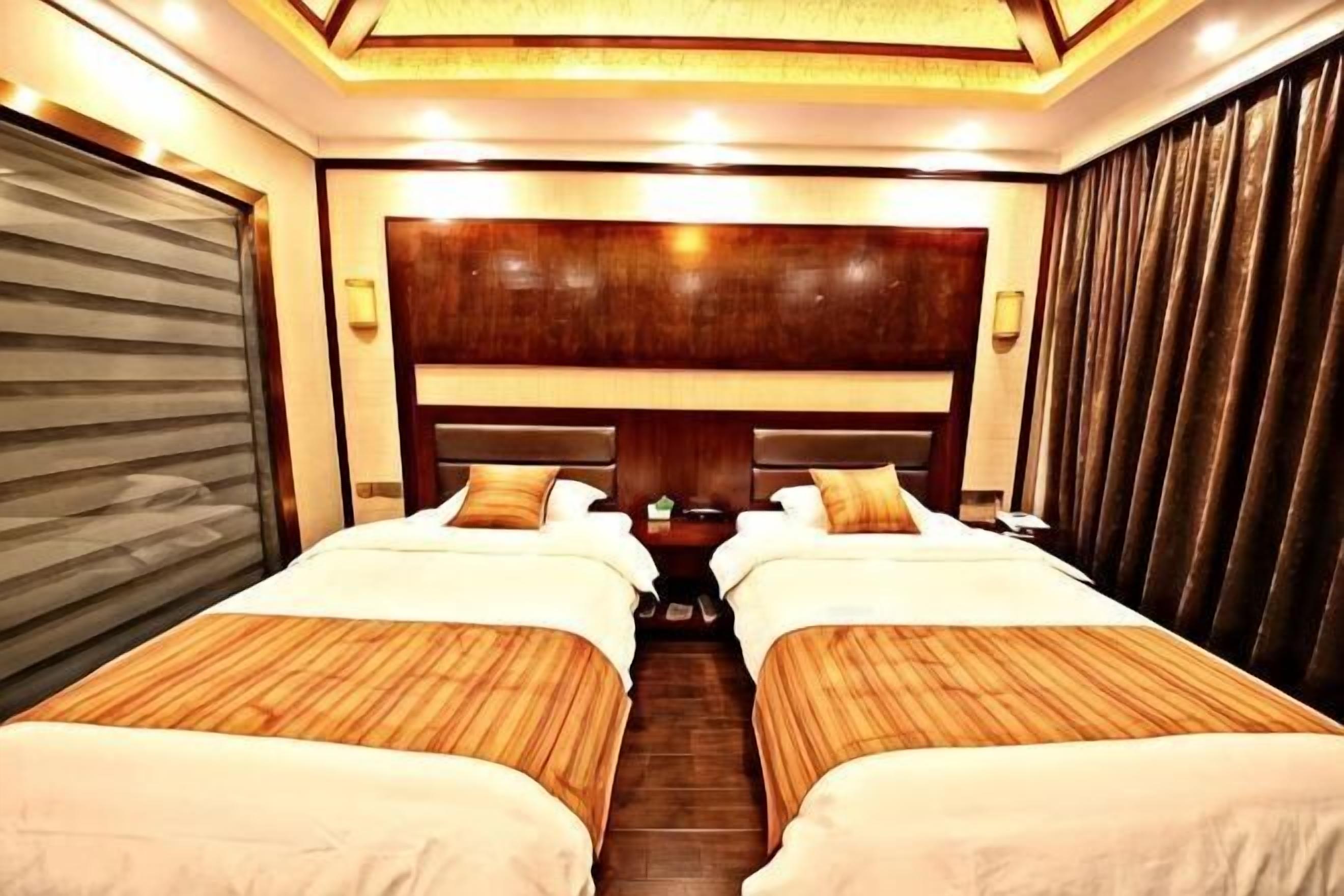 A hotel room with two beds, a wooden headboard, a closed sliding door, and a nightstand with a lamp.