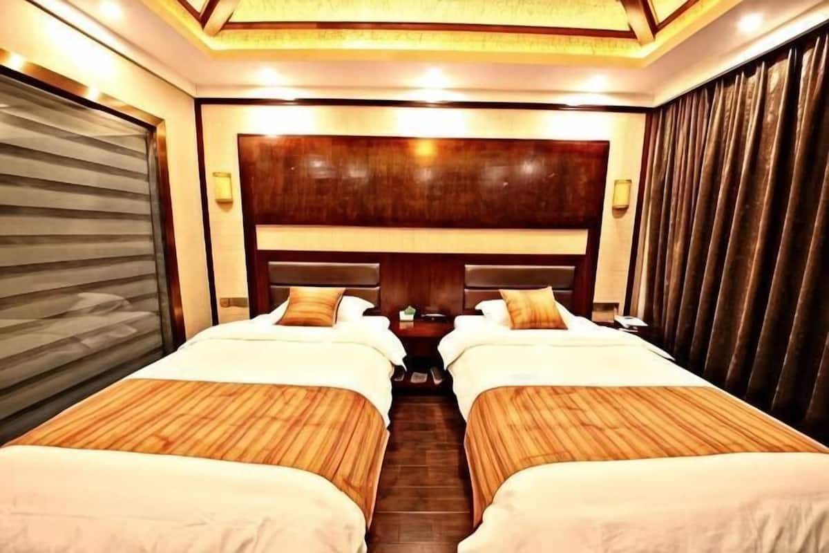 A hotel room with two beds, a wooden headboard, a closed sliding door, and a nightstand with a lamp.