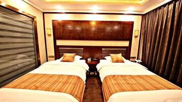 A hotel room with two beds, a wooden headboard, a closed sliding door, and a nightstand with a lamp.