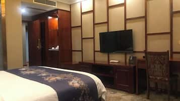 A hotel room with a bed, a TV mounted on a wooden panel wall, a desk, and a chair.