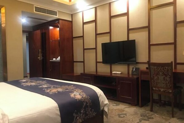 A hotel room with a bed, a TV mounted on a wooden panel wall, a desk, and a chair. - Dege Shandi Hotel (Dege)