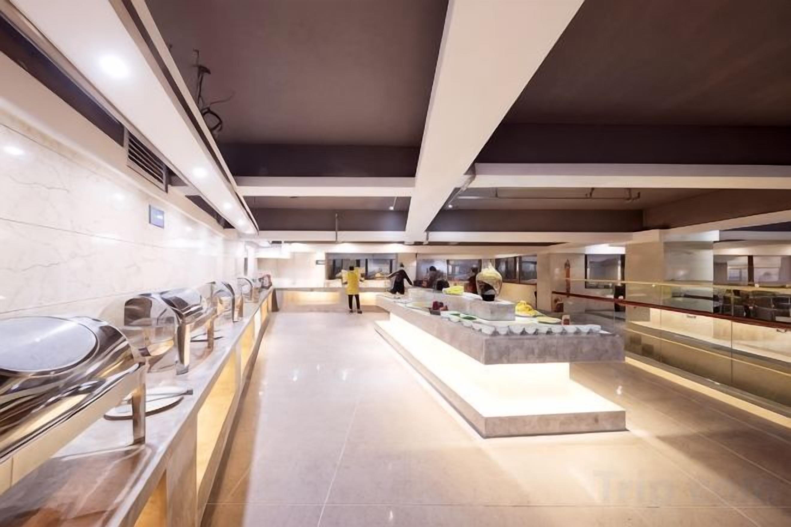 Un moderno vestíbulo de hotel con una larga barra de buffet, una isla central con exhibición de alimentos y un área de estar.