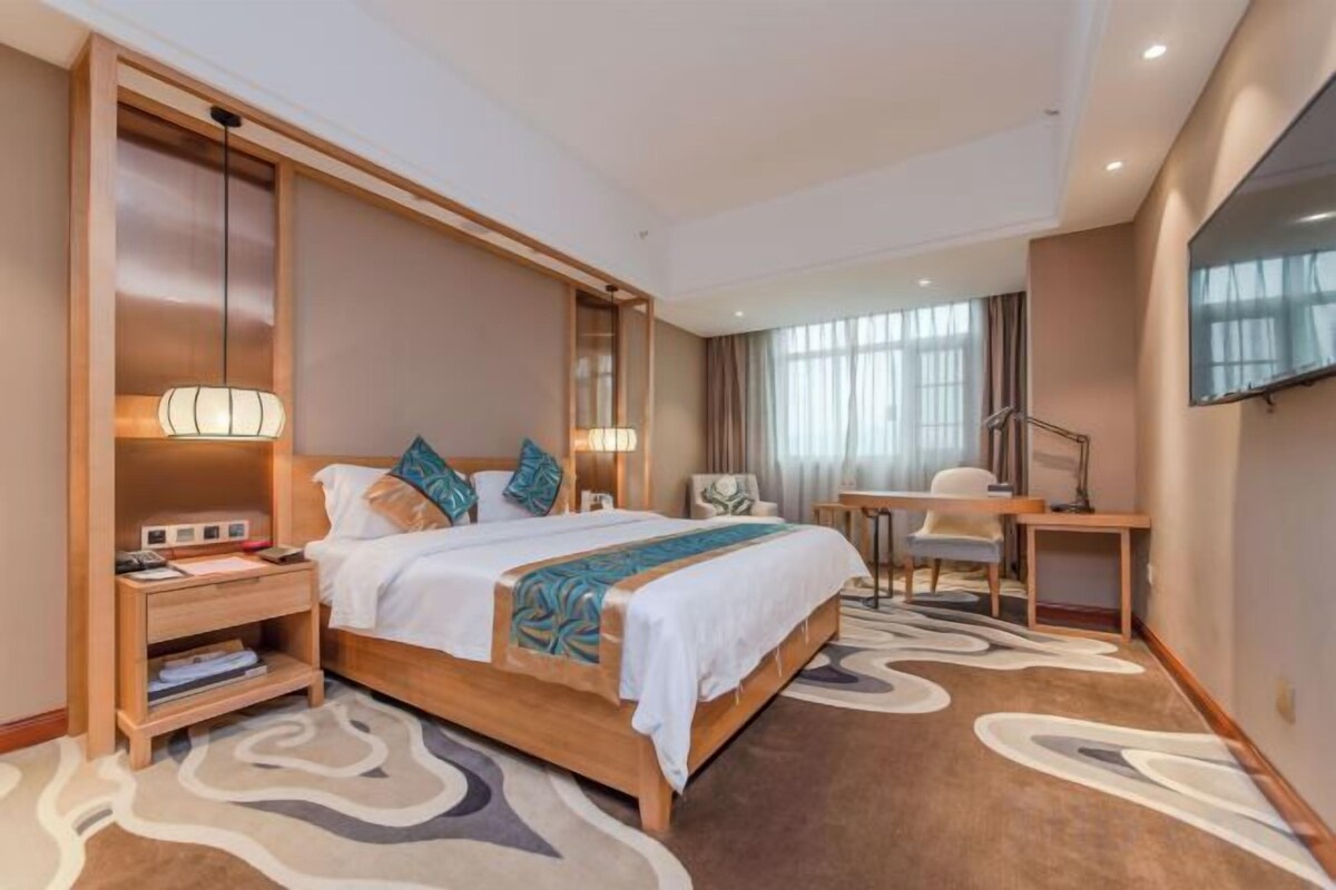 Quarto de hotel com uma cama grande, mesas de cabeceira, uma escrivaninha e televisão na parede.