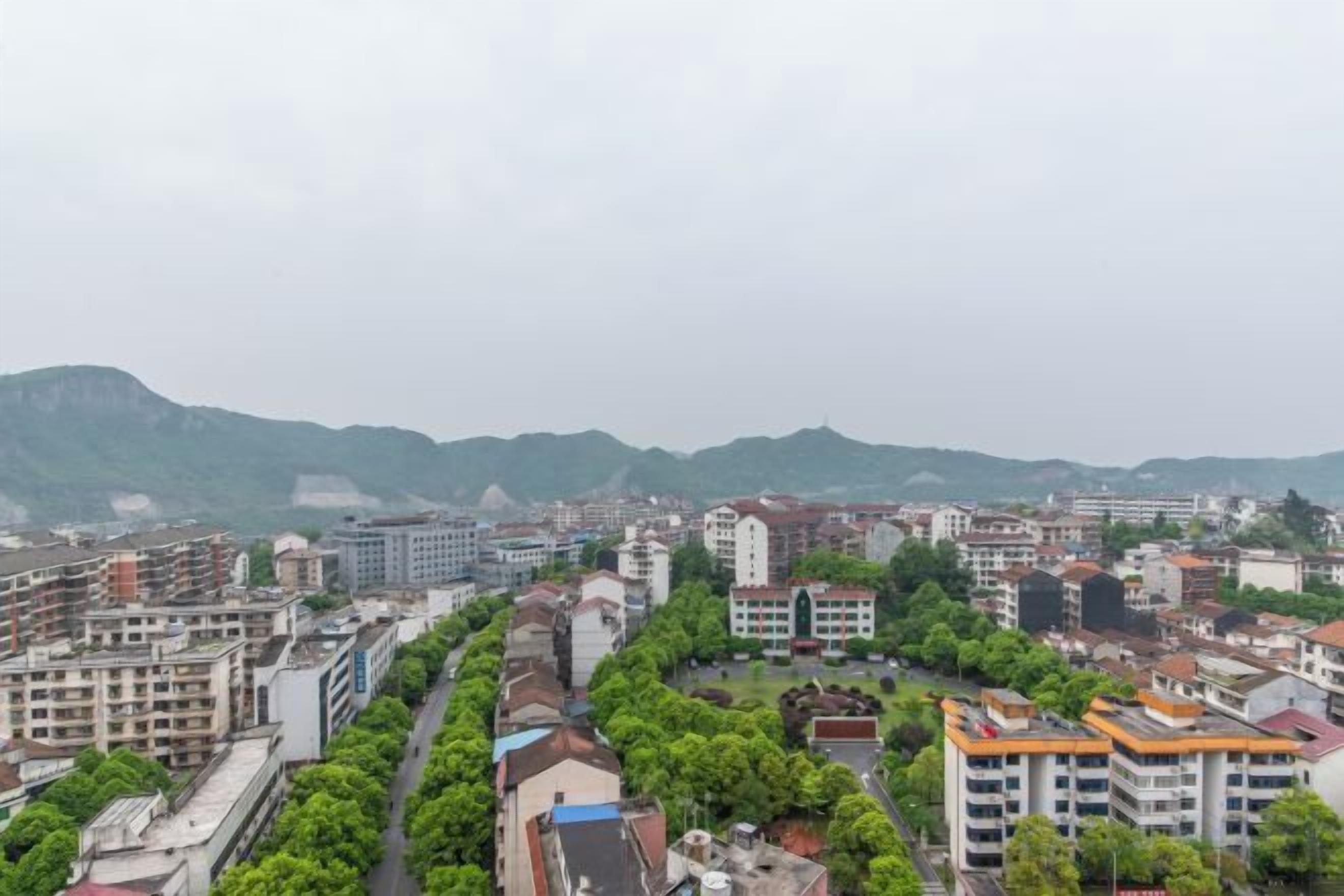 A cityscape with multiple buildings, a central road, and a mountainous backdrop.