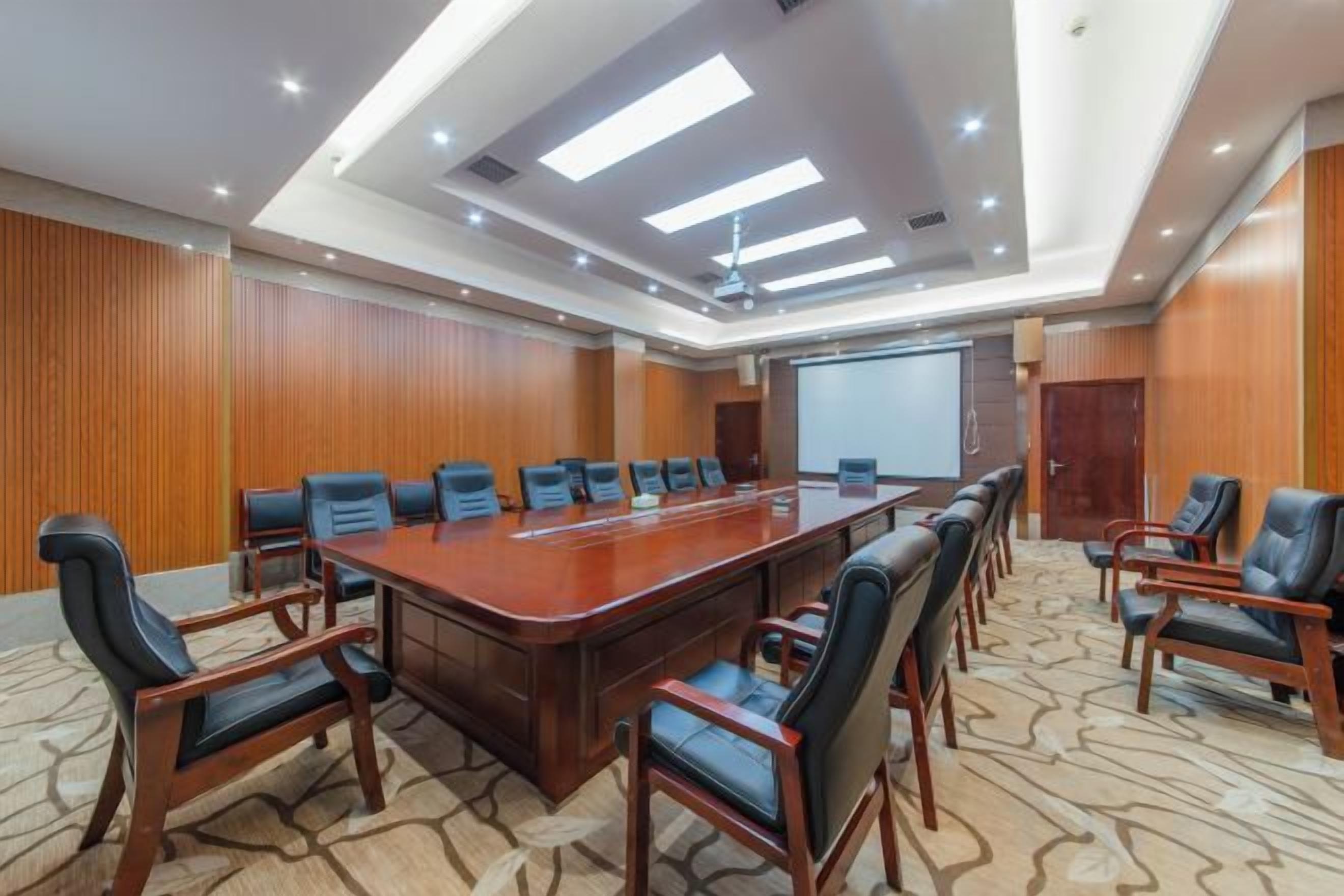 A conference room with a long table, chairs, a projector screen, and a carpeted floor.