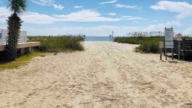 A sandy beach path leading to the ocean, with a palm tree and a wooden fence on the left, and a signpost on the right. - Relax in this cozy townhouse, 2block to the beach (Myrtle Beach)