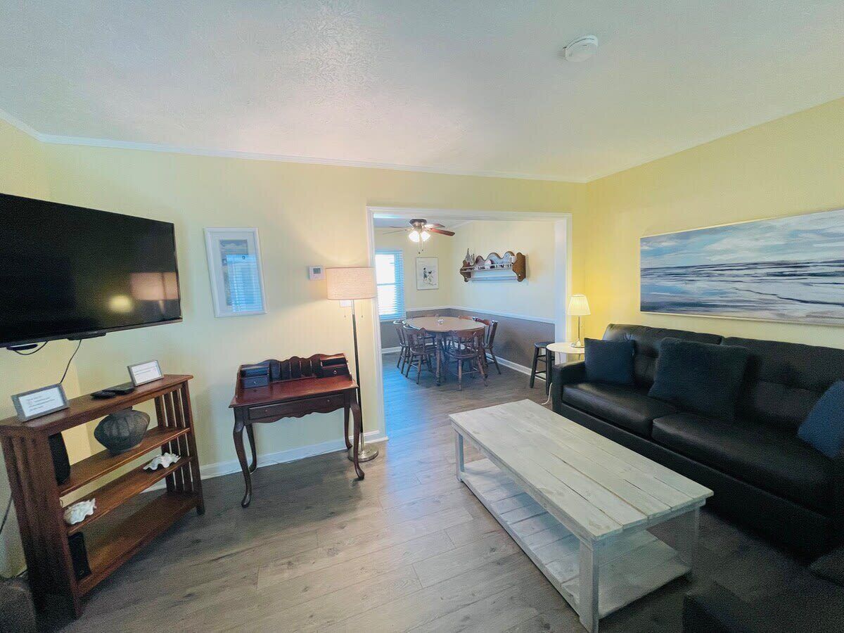 A living room with a flat-screen TV, wooden entertainment unit, a coffee table, a sofa, and a dining area with a round table and chairs.