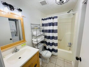 Et badeværelse med hvid vask, spejl, toilet og brusebad med stribet gardin.