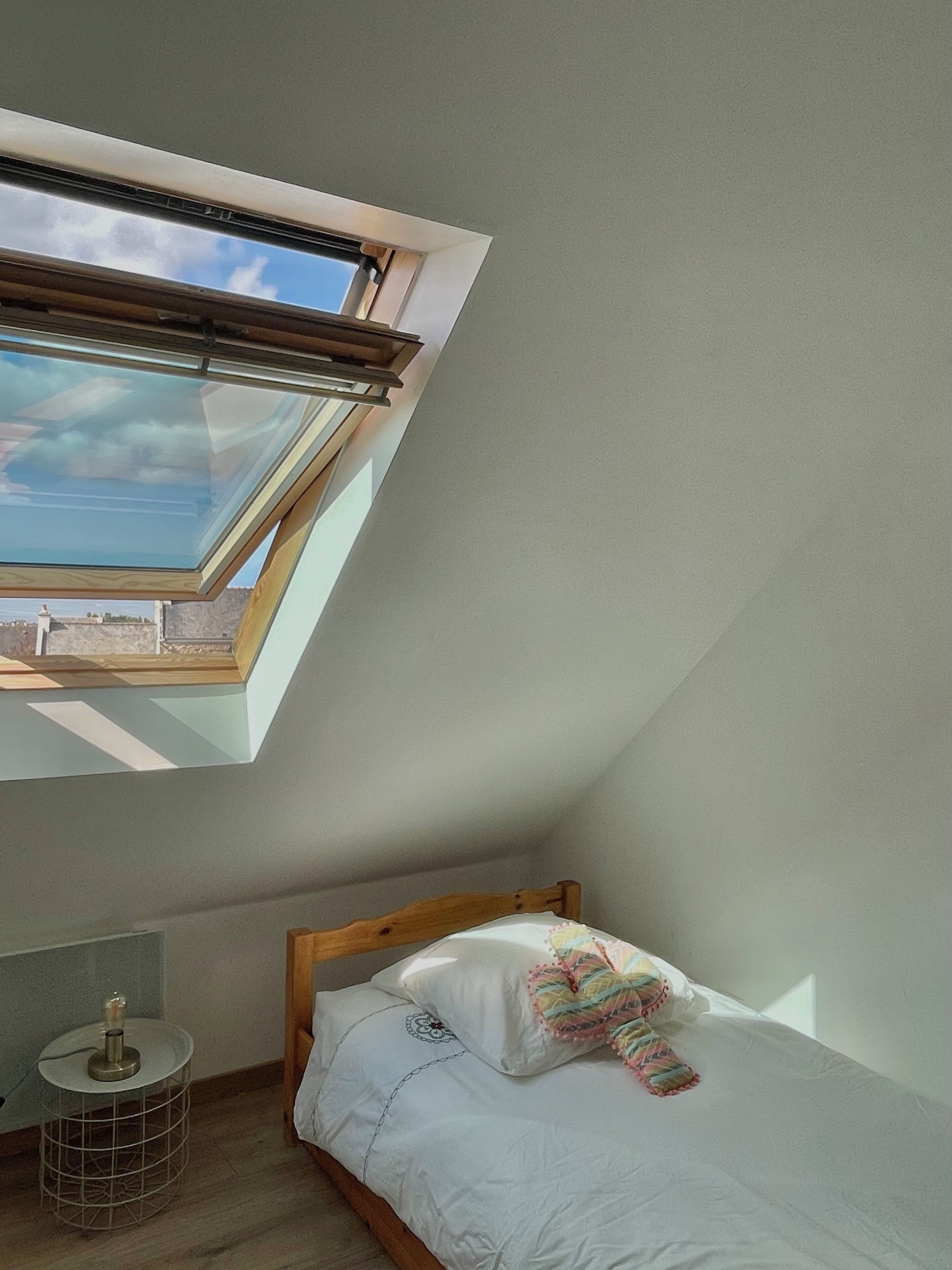A bedroom with a skylight, a bed, a bedside table, and a small round table with a lamp.