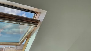 A bedroom with a skylight, a bed, a bedside table, and a small round table with a lamp.
