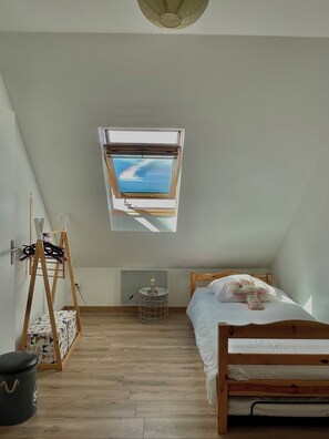 Un dormitorio de ático pequeño y bien iluminado, con techo inclinado, tragaluz, cama de madera, una mesita y una escalera.