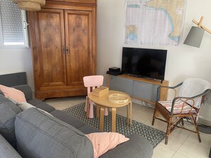 Un salón con un sofá gris, un mueble de madera, un televisor y un mapa en la pared.
