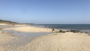 A sandy beach with footprints and rocks, and a clear blue sky.