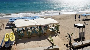 Un restaurante frente a la playa con terraza, sombrillas y kayaks.