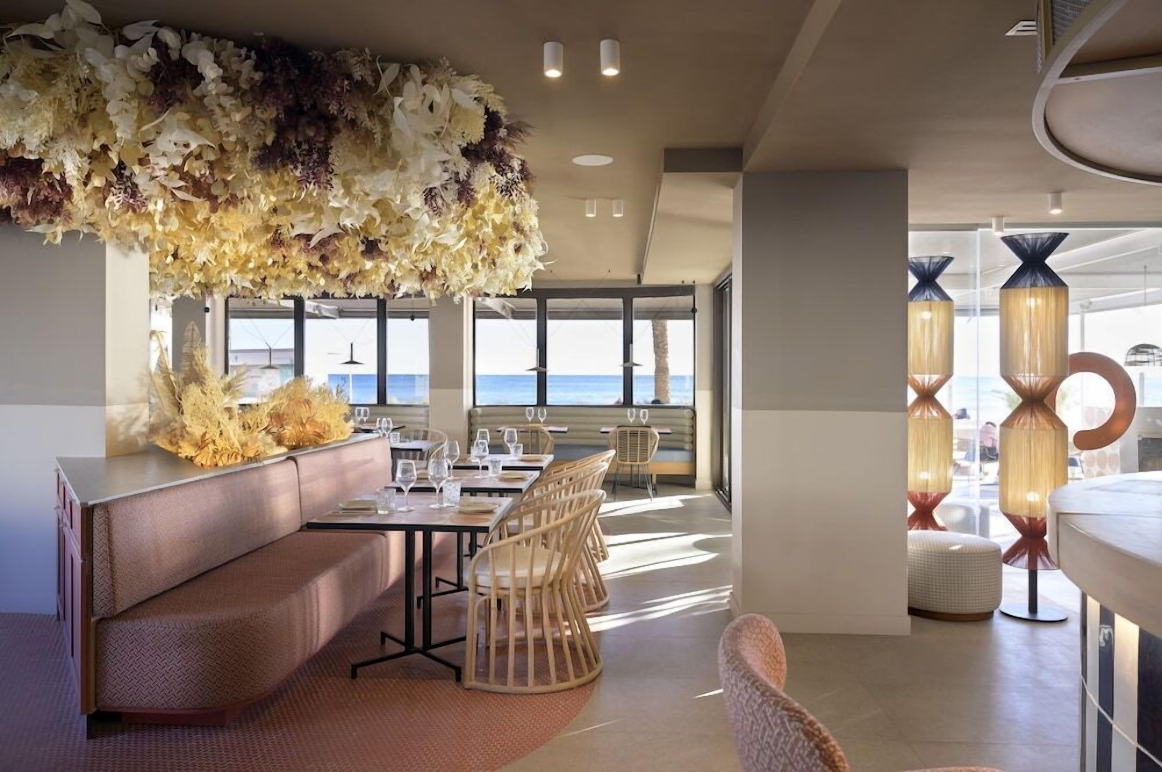 Un comedor moderno con un gran arreglo floral, un espacio de descanso con un sofá y sillones, y vistas al océano a través de amplios ventanales.