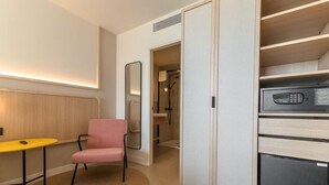 A compact hotel room with a kitchenette, a small seating area with a chair, and a mirror. - Akquaaa Boutique Hotel (Calafell)