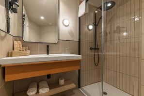Un bany modern amb dutxa envidriada, un lavabo blanc amb prestatge de fusta i un mirall a la part superior.