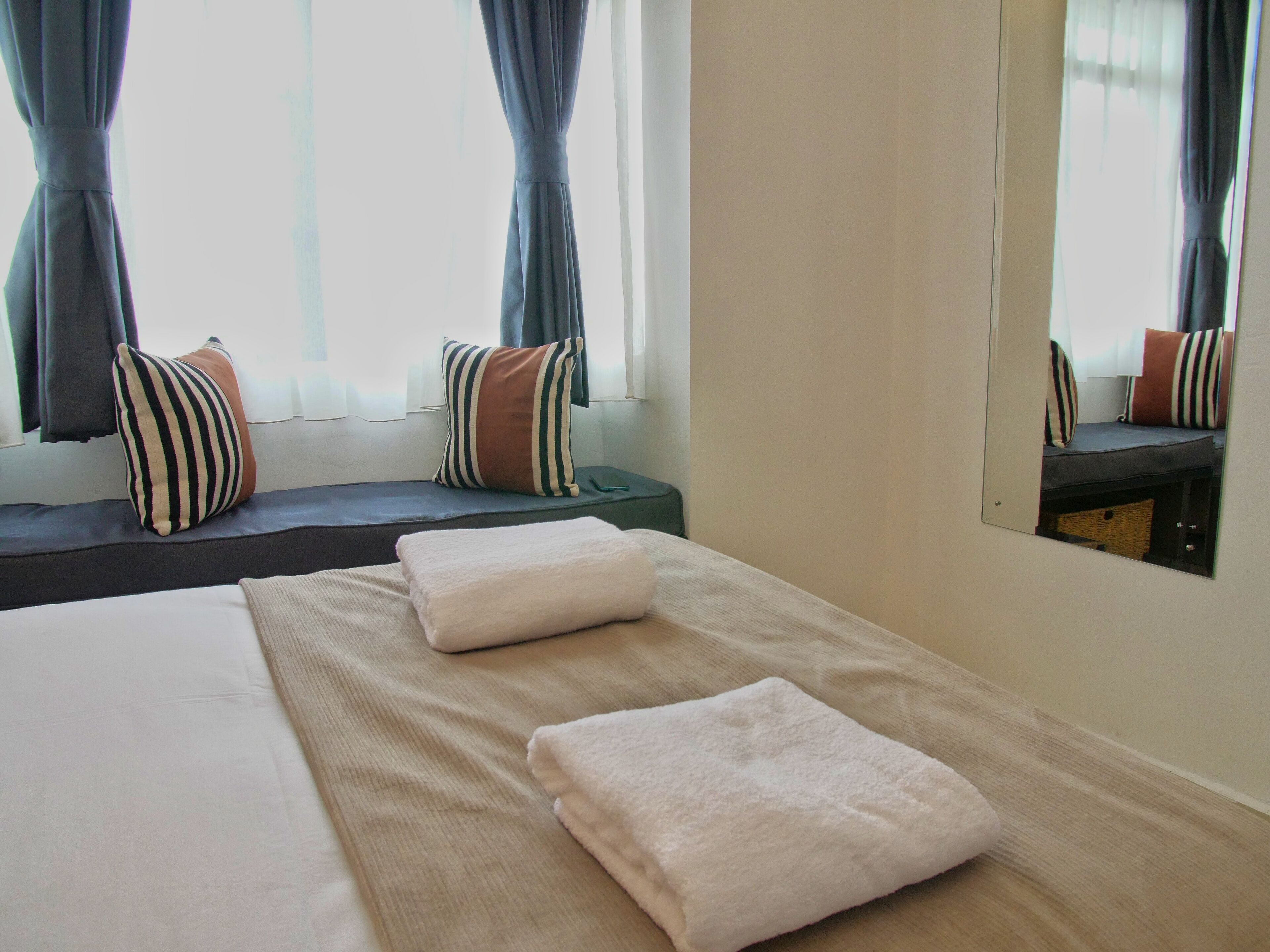 Une chambre d’hôtel avec un lit, un banc et une fenêtre avec des rideaux.