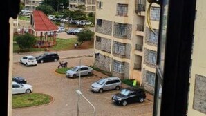 A view of a residential area with multiple apartment buildings, a parking lot with cars, and a clear sky. - Zendo Suite (Nairobi)