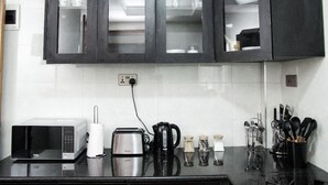 A kitchen with dark cabinets, a microwave, toaster, coffee maker, and various utensils. - Zendo Suite (Nairobi)