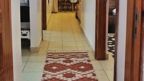 A hallway with a patterned rug, wooden doors, and a dining area with a clock on the wall. - Zendo Suite (Nairobi)
