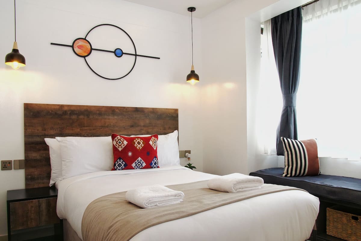 A neatly made bed with a wooden headboard, two bedside lamps, and a wall clock.